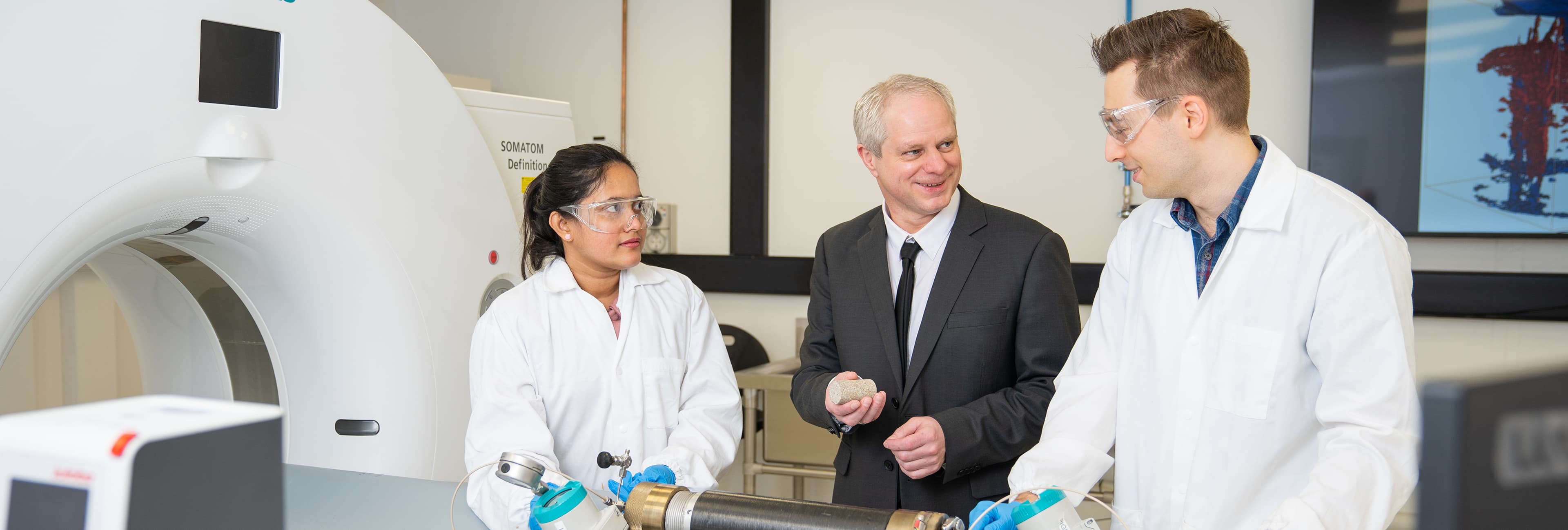 Woman and man in white lab coats speaking to another man in blue suit