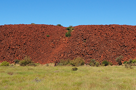 Hill of red rocks with green grass in the foreground and blue skies.