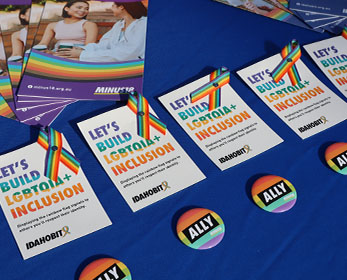 ALLY badges, IDAHOBIT ribbons and IDAHOBIT pamphlets are laid out at an event stall.