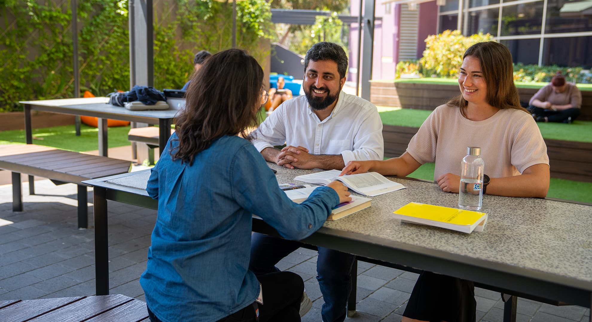 A group of Edith Cowan University students are chatting and going through a textbook.