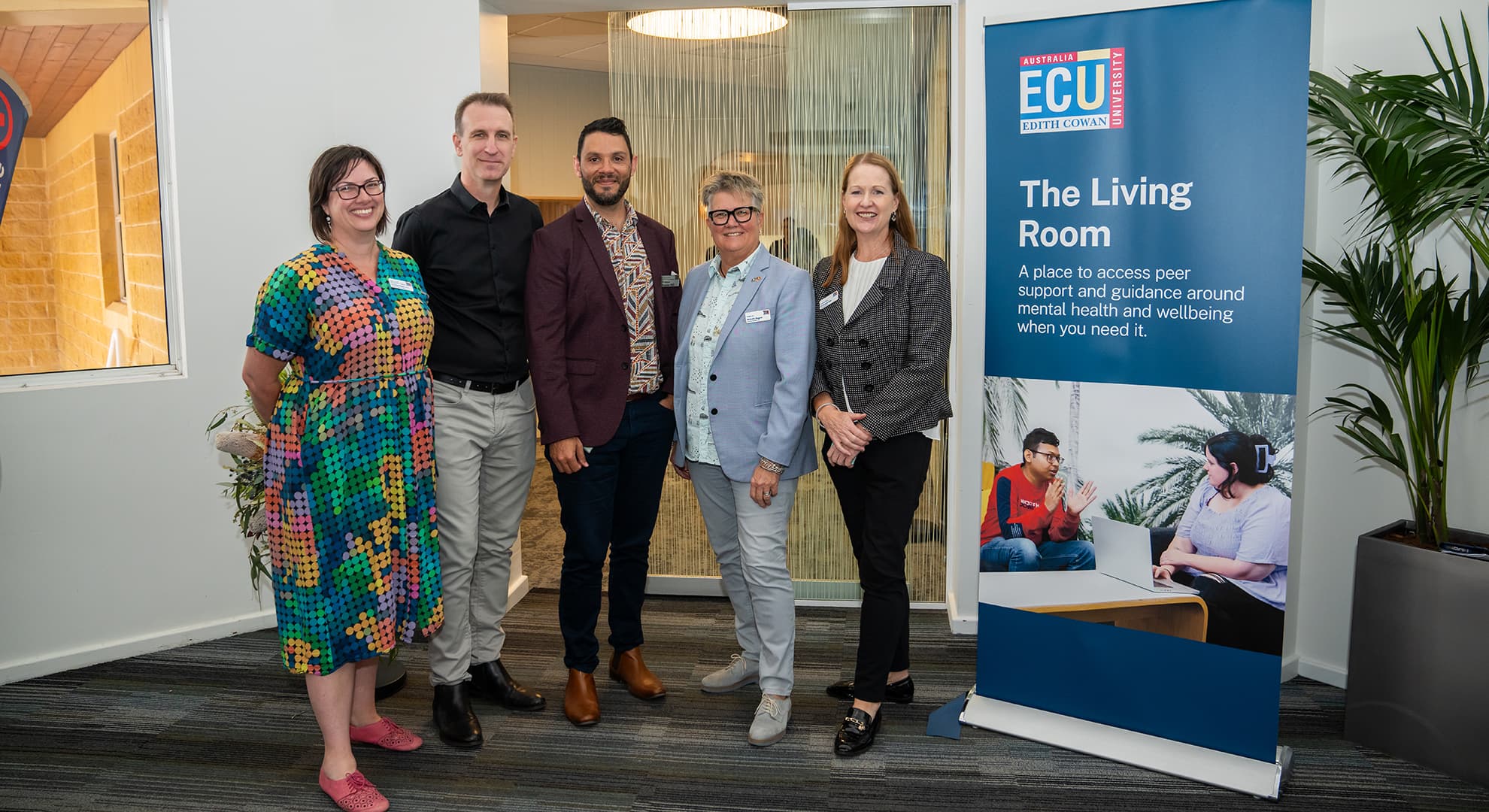 Five ECU staff standing in entryway with The Living Room banner on the right side of the image