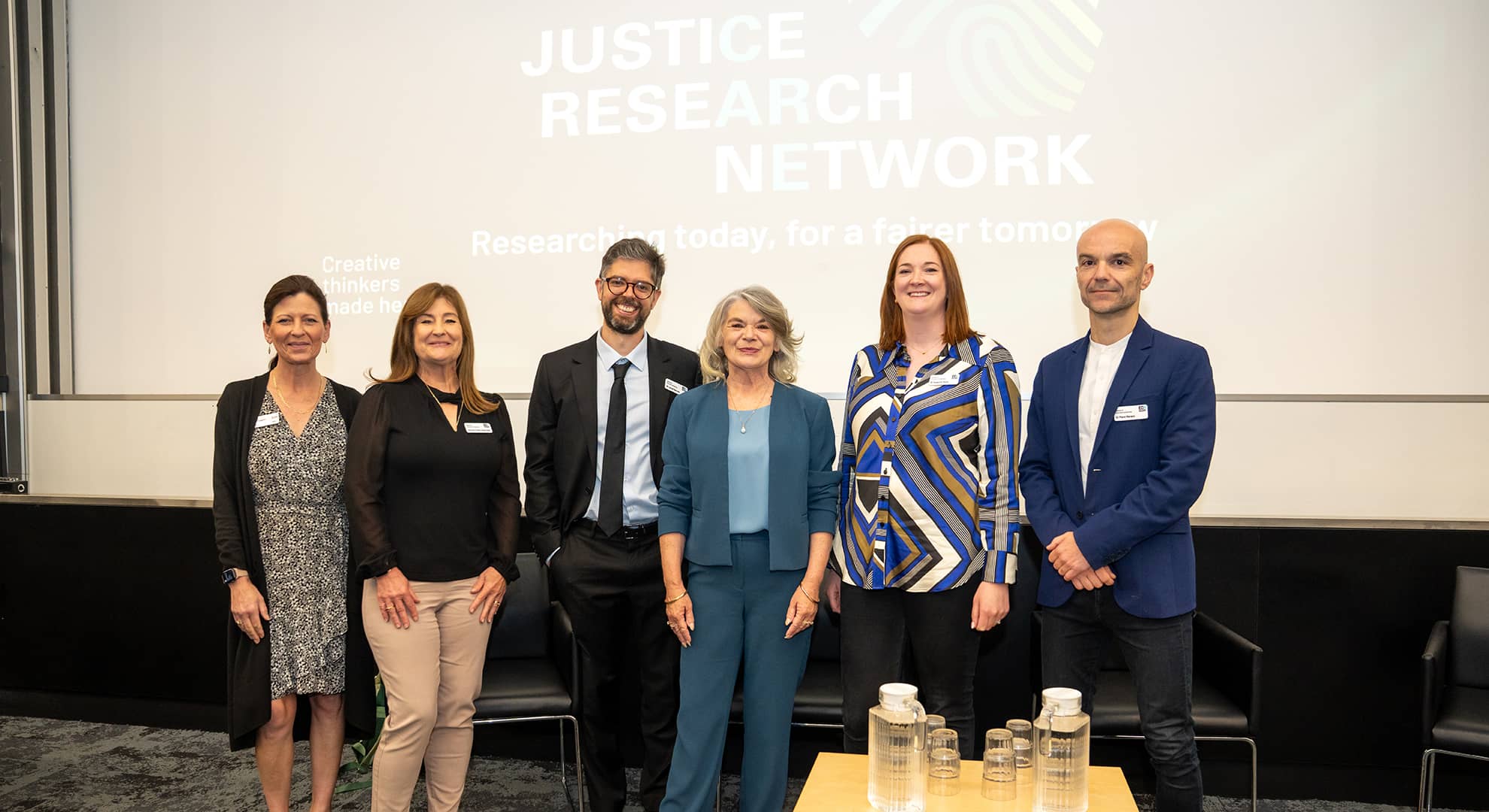A group shot of six people posing in front of a large screen