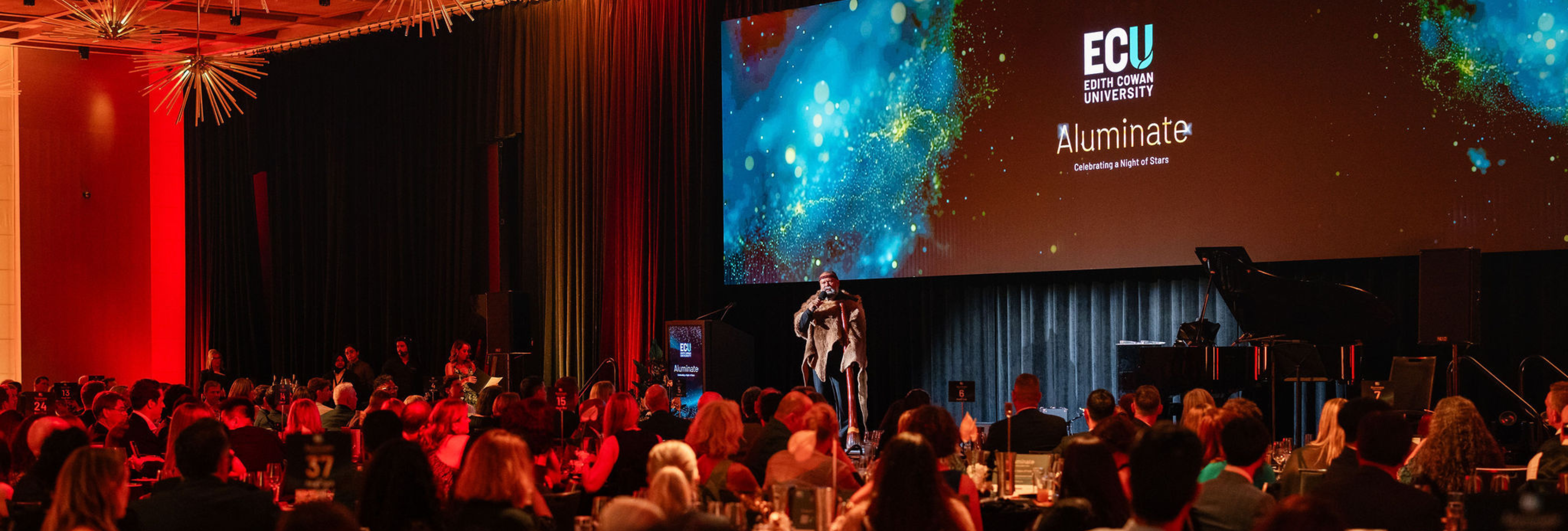 Aluminate 2025 room full of people with Aboriginal Elder on stage performing Welcome to Country