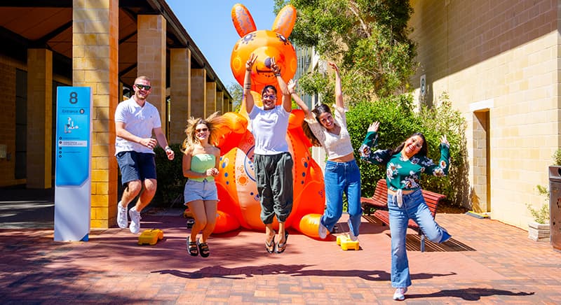 A group of students on campus jumping in front of a large inflatable kangaroo