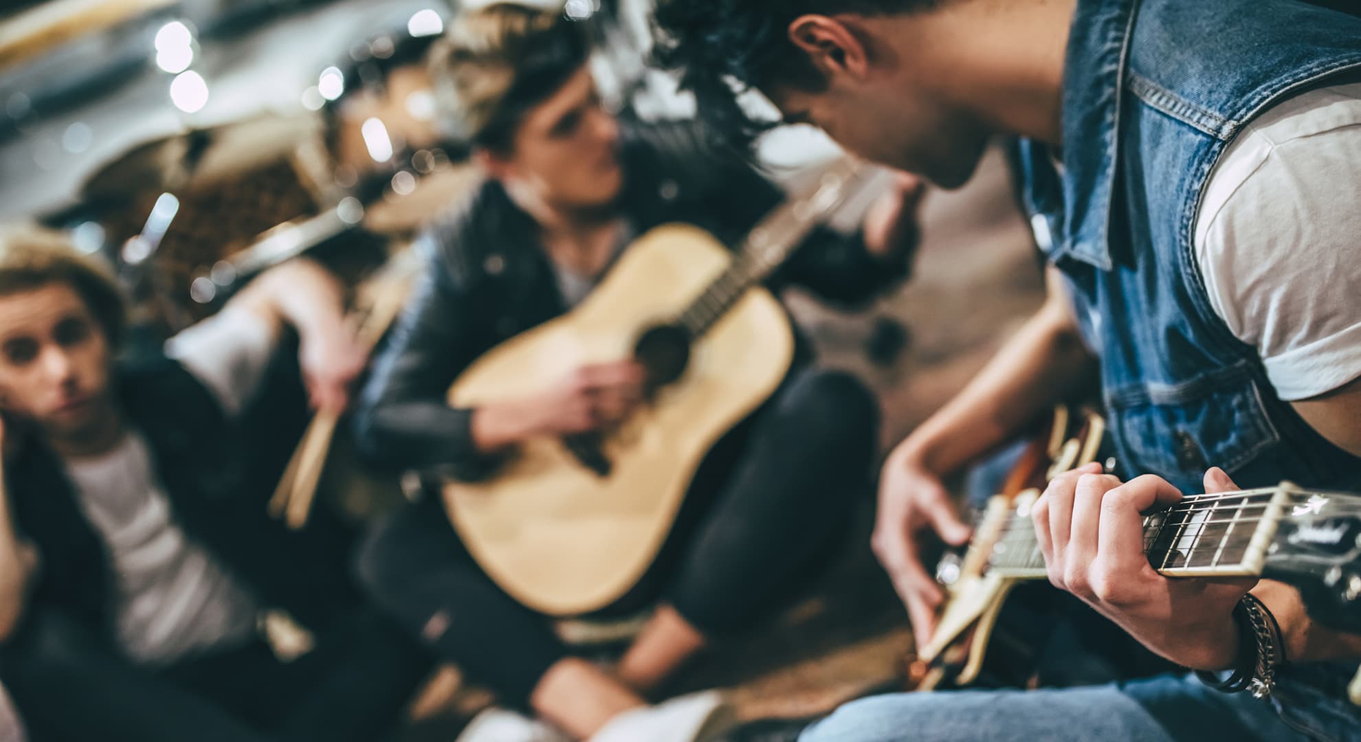 Close up shot of community rock music band. Guitar players and drummer are sitting on the floor at rehearsal base.