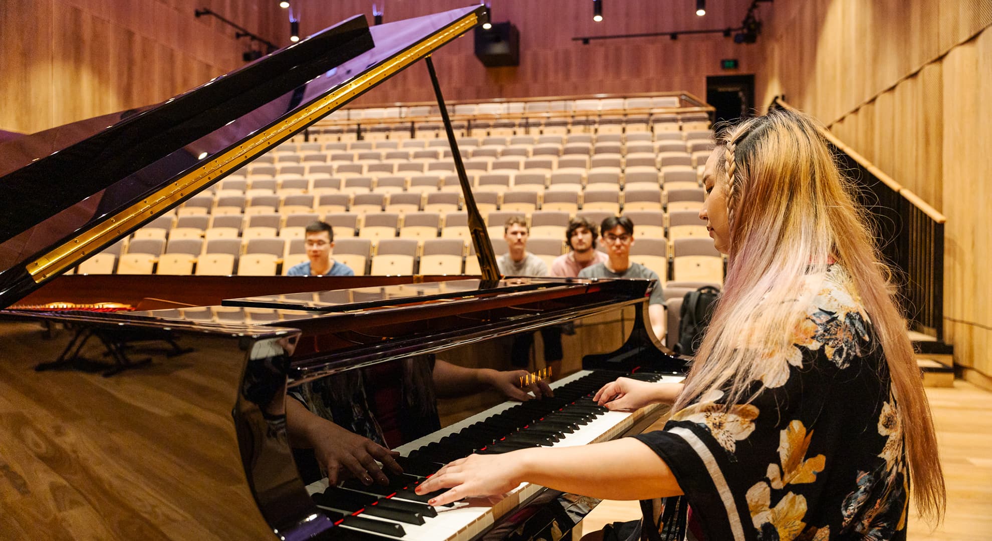 A woman plays a grand piano in a WAAPA studio as four others look on