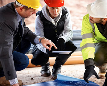 Professional workers looking at the iPad and blueprints on a work site..