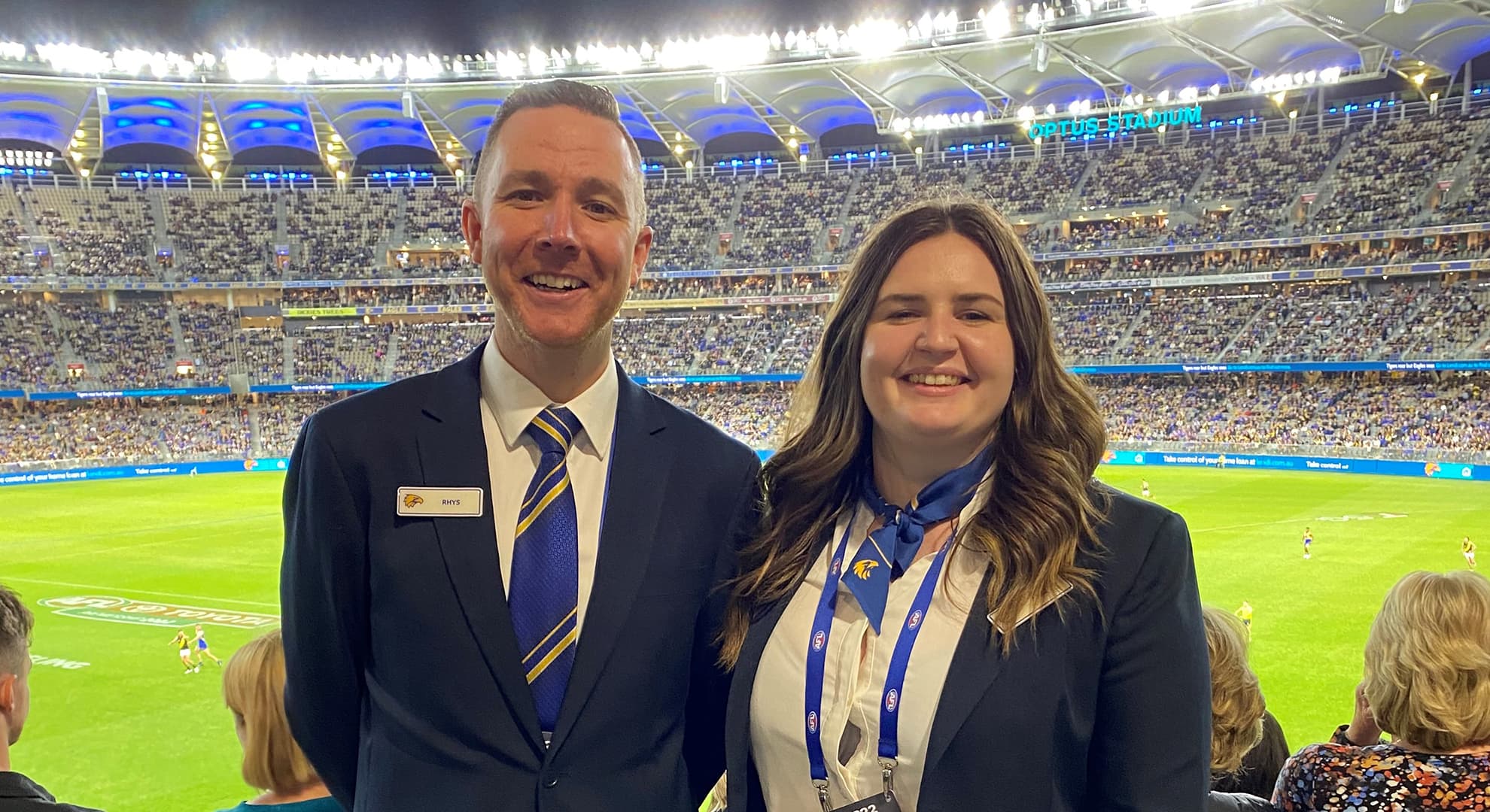 Male and female standing in the audience in a busy sports stadium