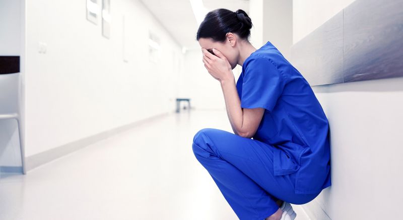 Nurse kneeling in a hospital hallway with her head in her hands.