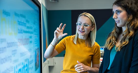 Two women standing in front of large computer screen