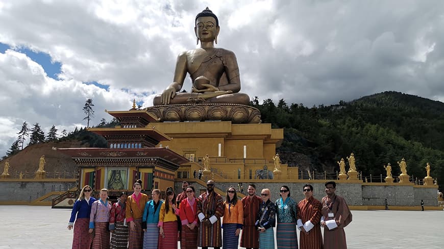 Male and female students posing in front of a Bhutanese statue