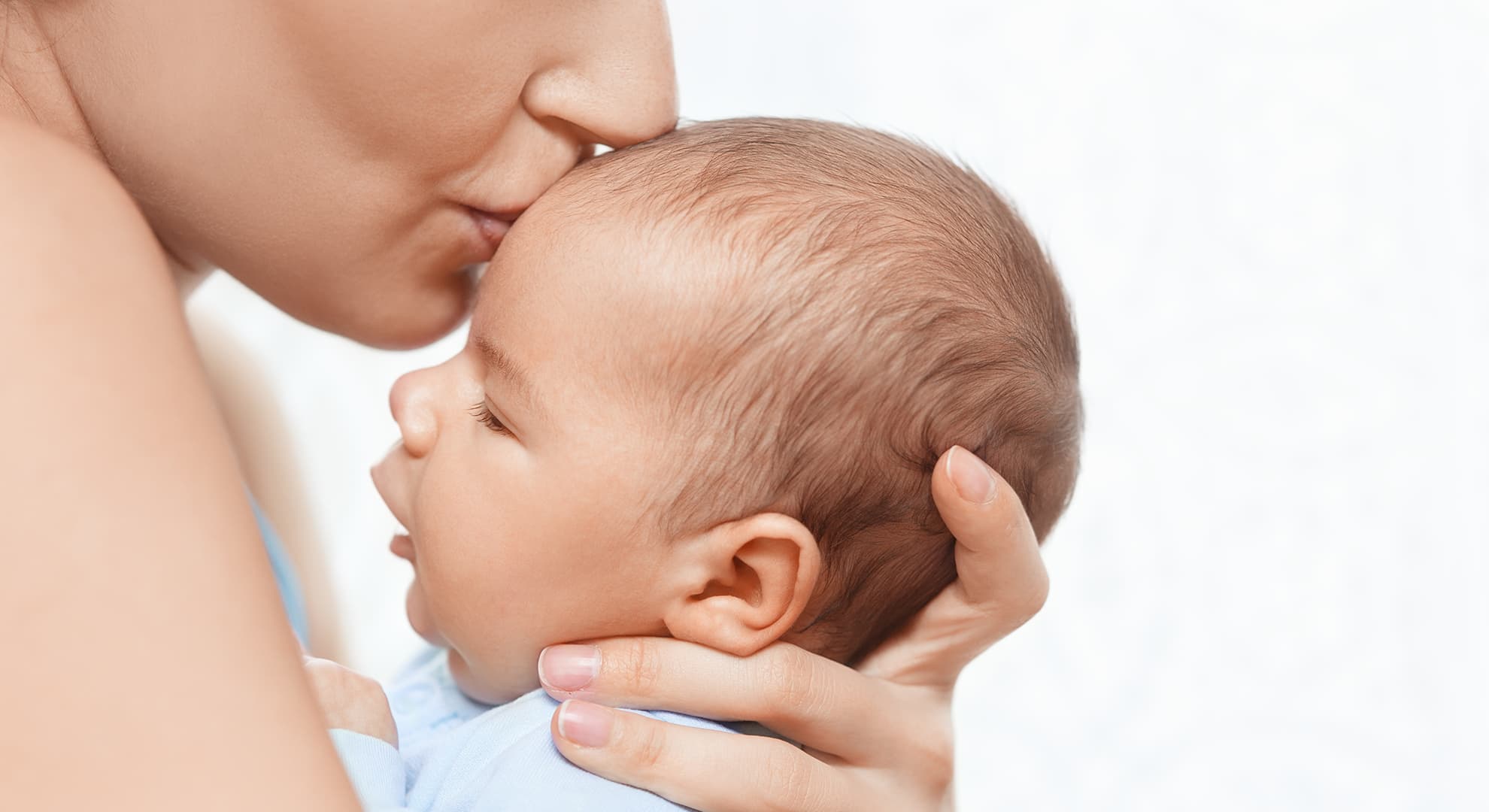 Woman holding a baby and kissing its forehead