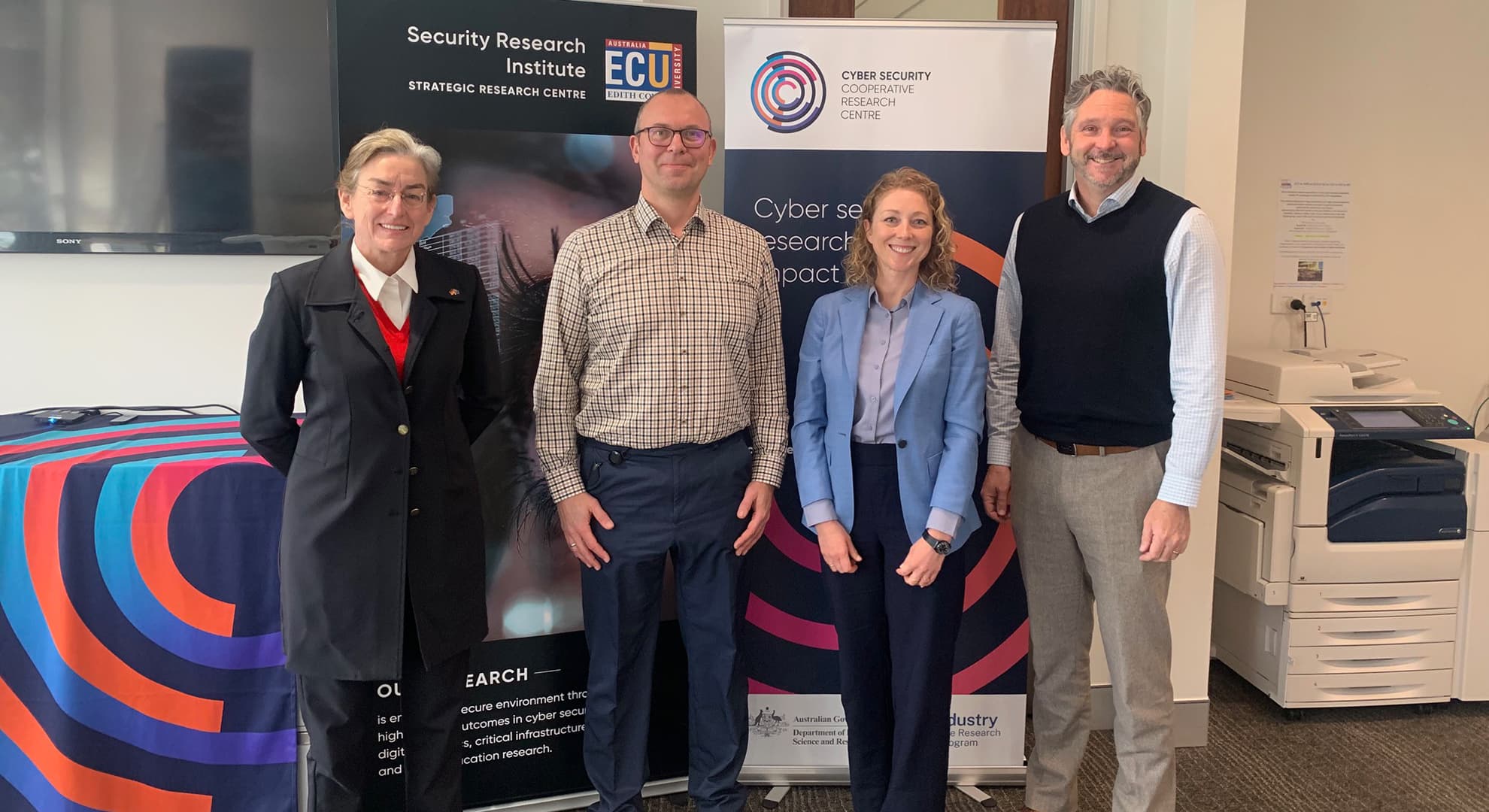 Researchers and embassy representatives stand in front of a pull up banner