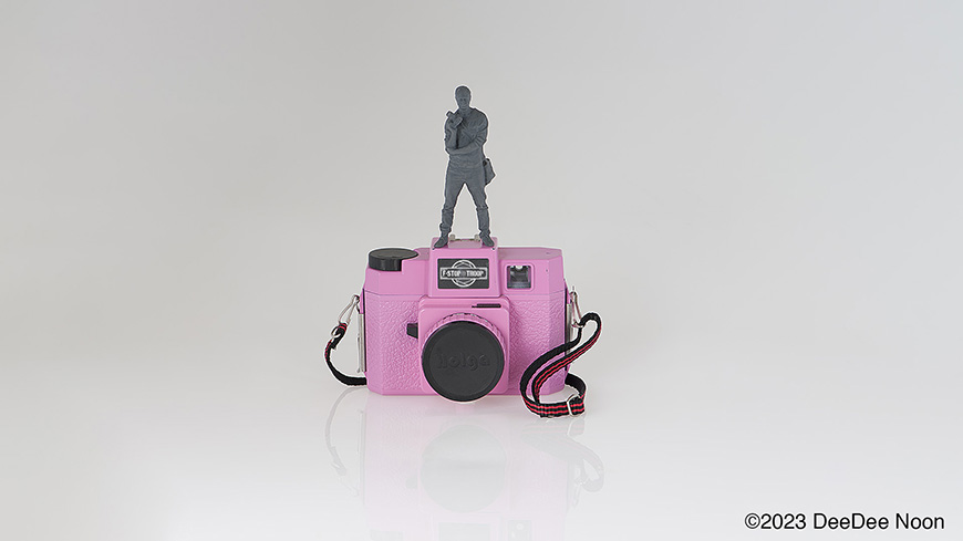 Toy figure standing on top of pink camera.