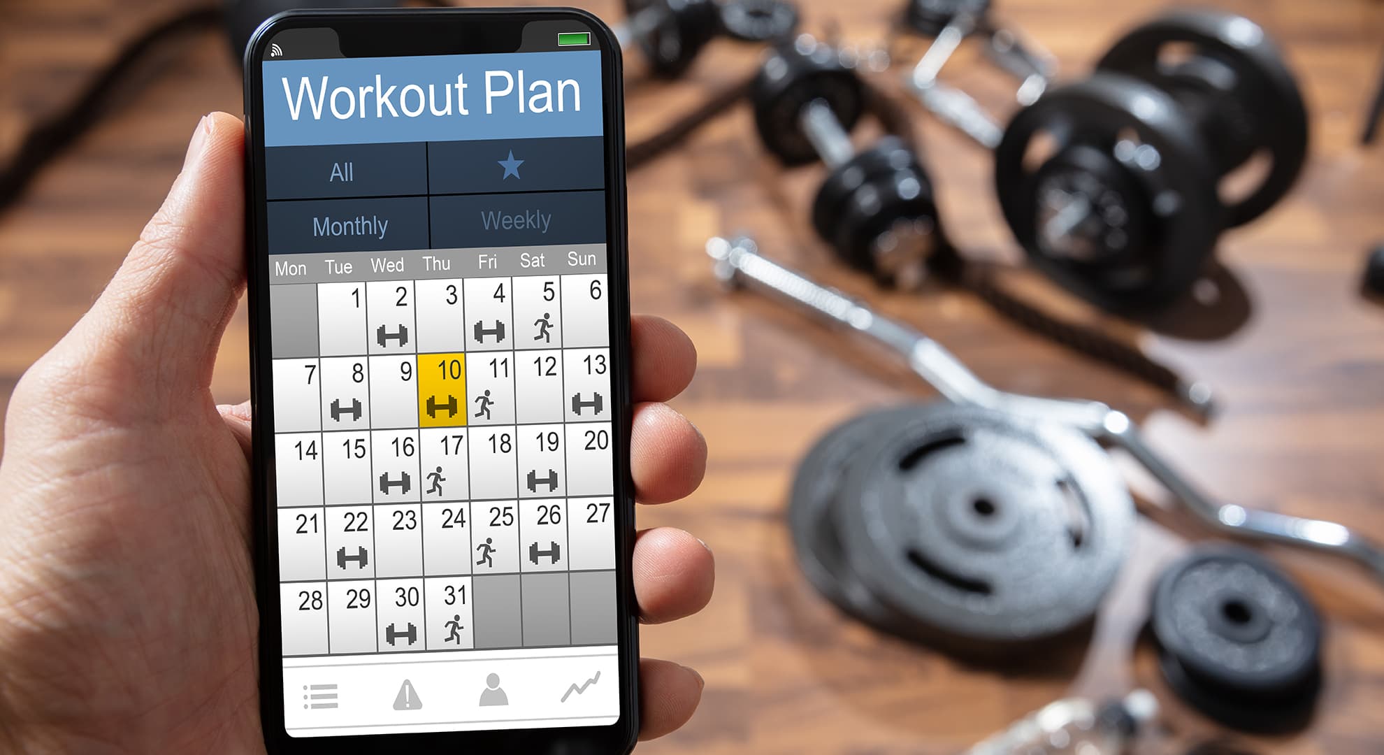 Person looking at workout plan on their phone, with gym equipment in the background.
