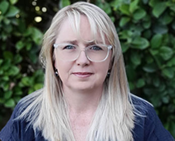 A portrait photo of Rebecca Lowe standing in front of foliage