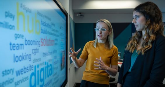 Two woman standing at a digital information board.