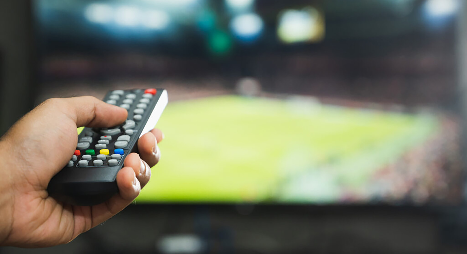 Image of a TV remote pointing towards a sports broadcast on TV.