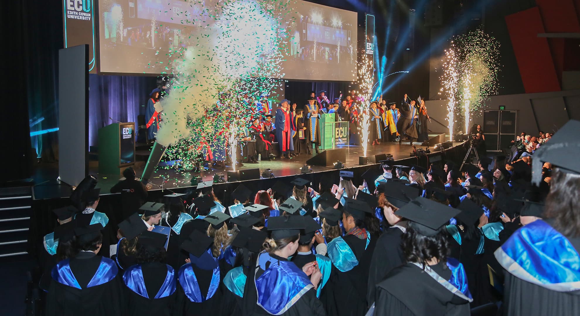 Students on a stage with fireworks.