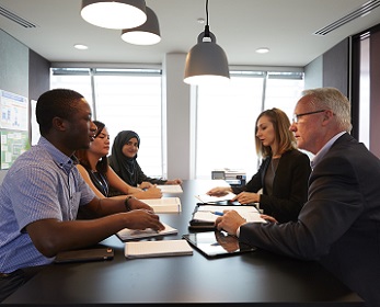 Five adults sitting around a table discussing paper infront of them.