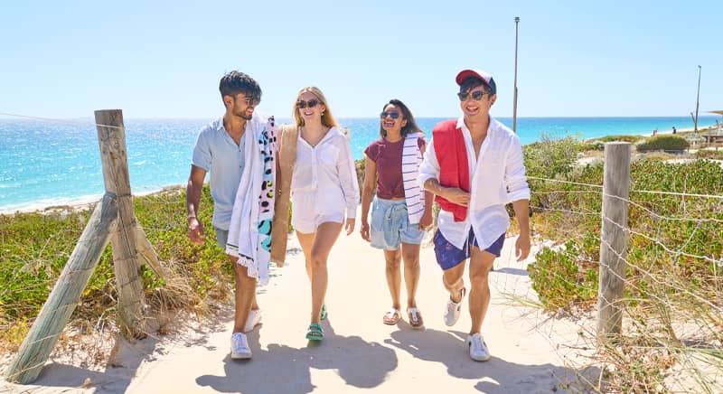 Four students walk up beach holding towels
