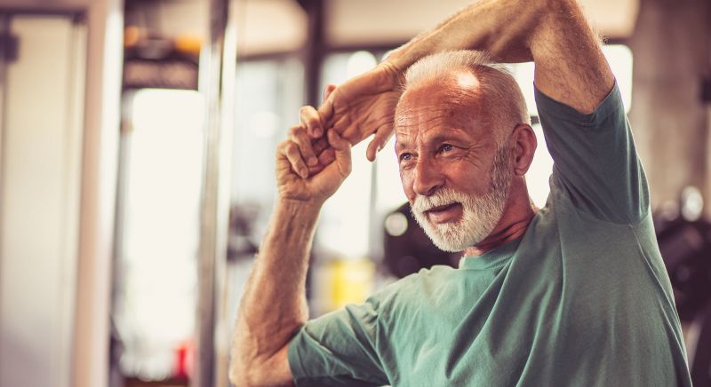 A grey haired man stretching his arm over his head