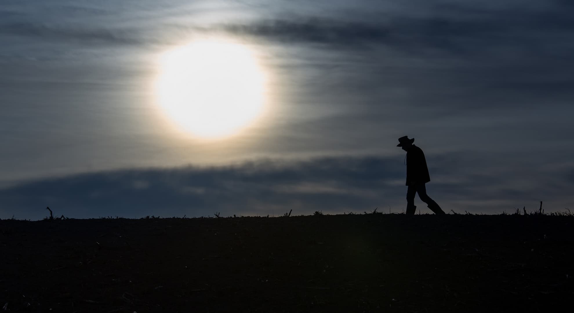 Silhouette of a farmer in a field with the sun low in the sky.