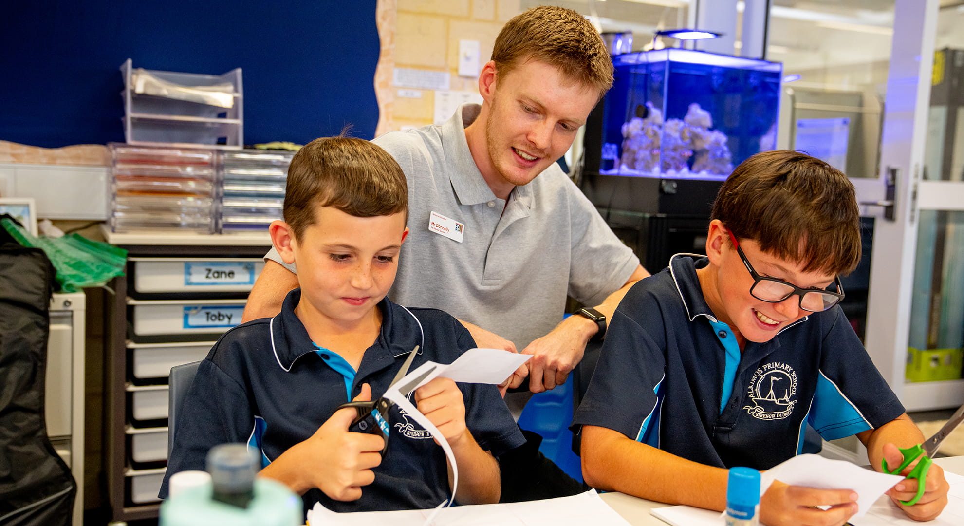 Teacher helping two young students at desk.