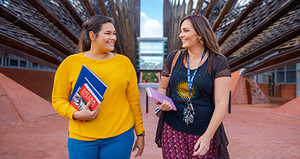 Two women holding text books and walking in between building 1 on ECU Joondalup campus