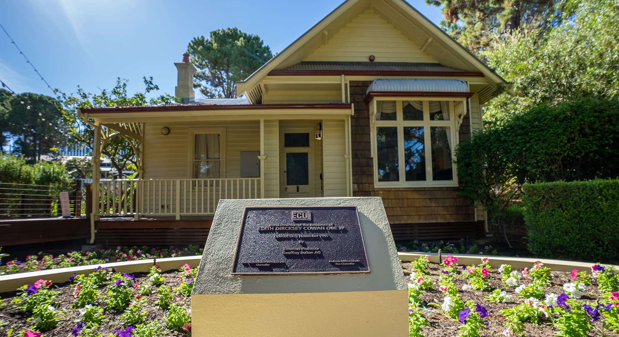 Small cottage in a garden on a university campus with plaque in the foreground.