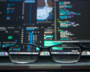 A pair of reading glasses has been placed on a computer desk in front of a monitor showing an edit software interface in soft focus.