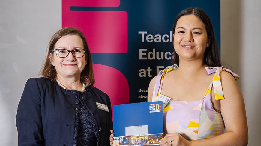 Janice Simons wears a purple and yellow summer dress and smiles, holding her certificate with Professor Caroline Mansfield at the School of Education Prize Giving Ceremony.