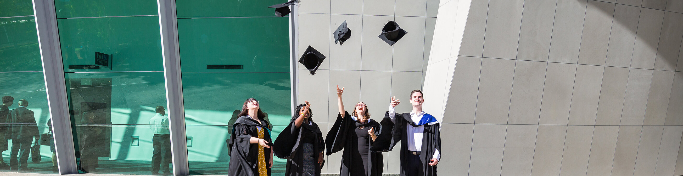 Four students wearing full regalia, throwing their mortar board hats in the air
