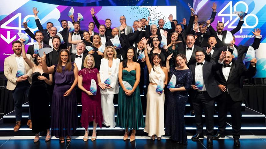 A group of business and community leaders throw their hands up in celebration on a stage.