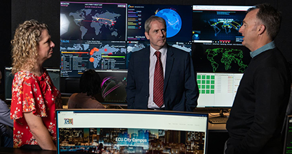 Three people having a discussion in a newsroom