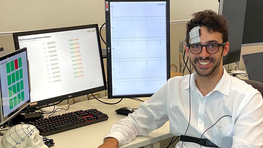 Oliver Guidetti at desk with computer screens and brain scanner on his head