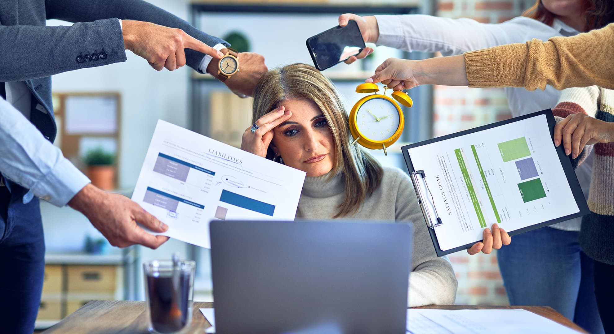 Woman at desk with people holding various objects in front of her face.