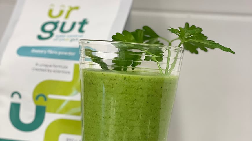 A green drink and a pouch of ur gut resting against a wall.