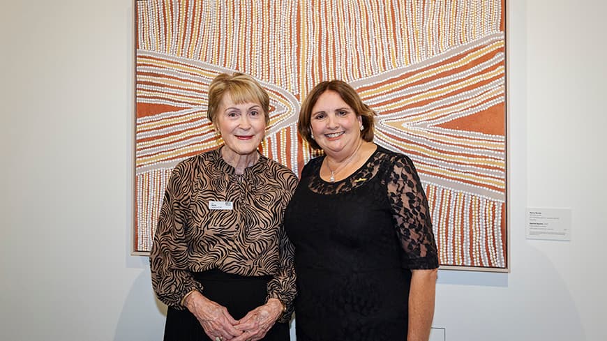 Two women standing together in front of artwork