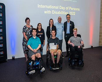 A group of ECU students and staff are standing in front of a screen with the words 'International Day of Persons' with Disabilities 2022'. Three students at the front of the group are using wheelchairs.