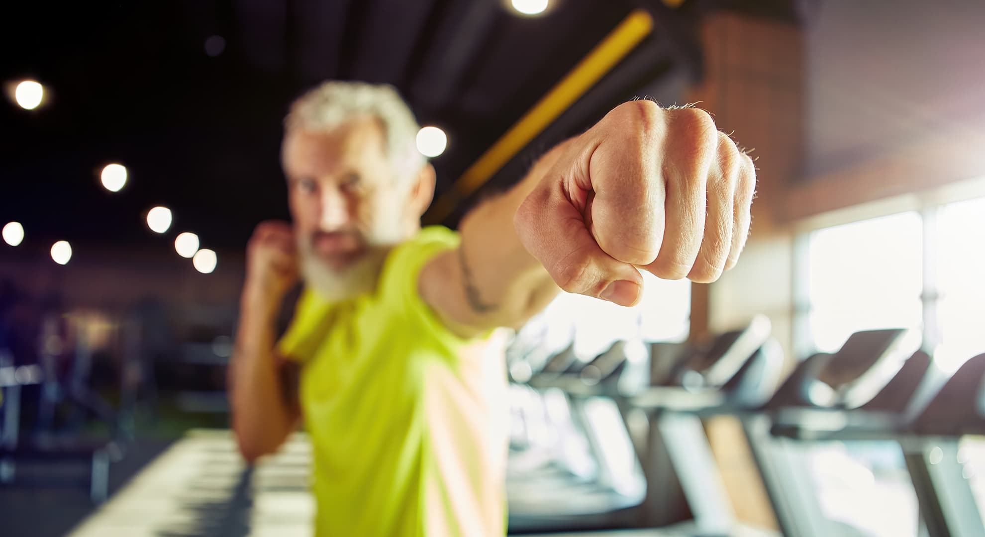 Older man in a gym posing with his fist towards the camera