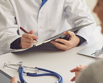 A person in a white lab coat holds a clipboard and a stethoscope.