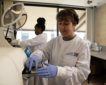 Image of a female PhD student working in a lab with a white lab coat on