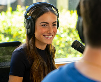 A student learns the broadcasting ropes in ECU’s radio studio. They are wearing headphones and seated in front of a microphone.