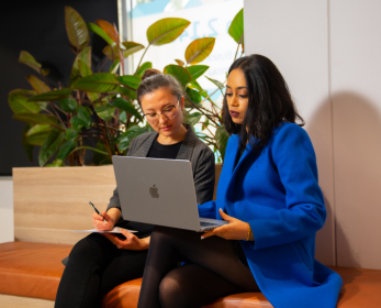 Two ECU students sitting together and looking at a laptop screen while studying. One student takes notes as they review online reading materials, representing digital access to Taylor & Francis eTextbooks and eBooks.