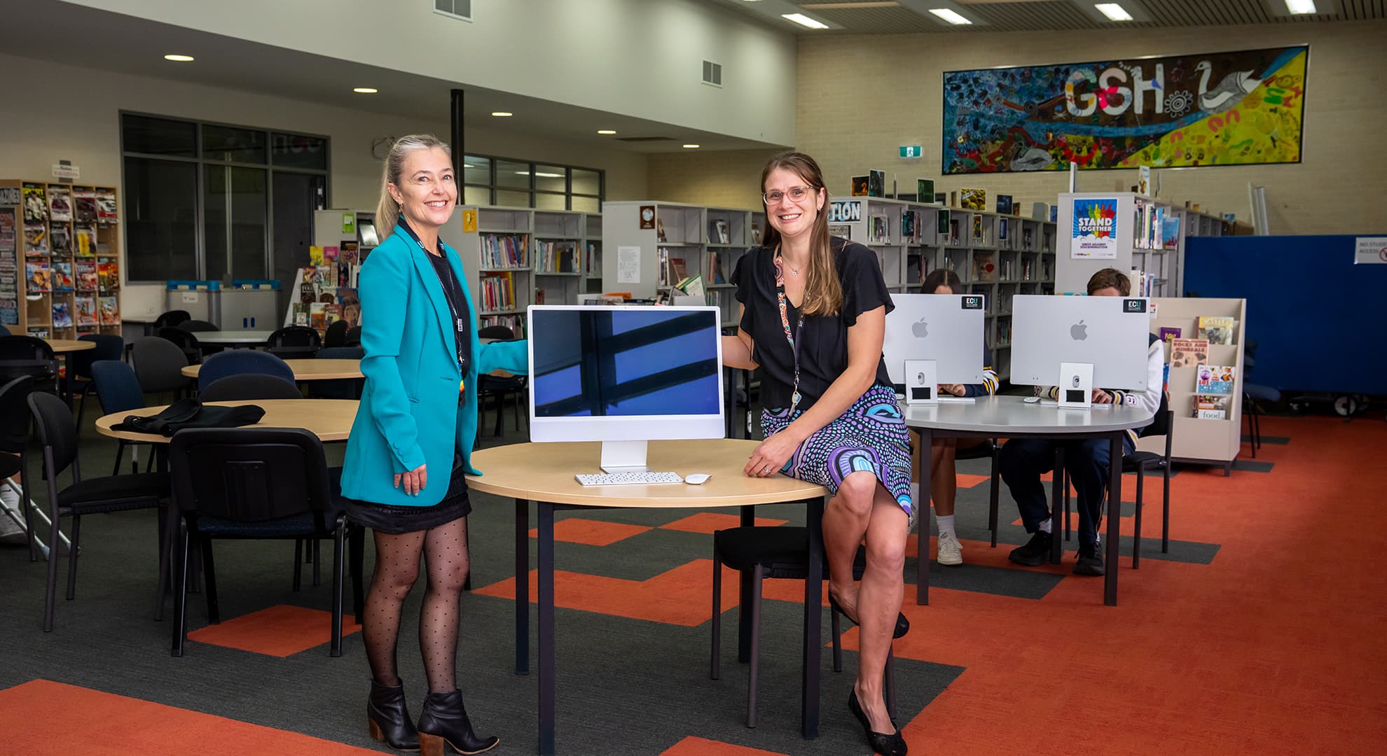 Two women standing next to computers with two students.