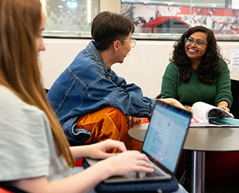 Students sit and chat in a collaborative space at the Mount Lawley Library. A third students works on their laptop in the foreground.