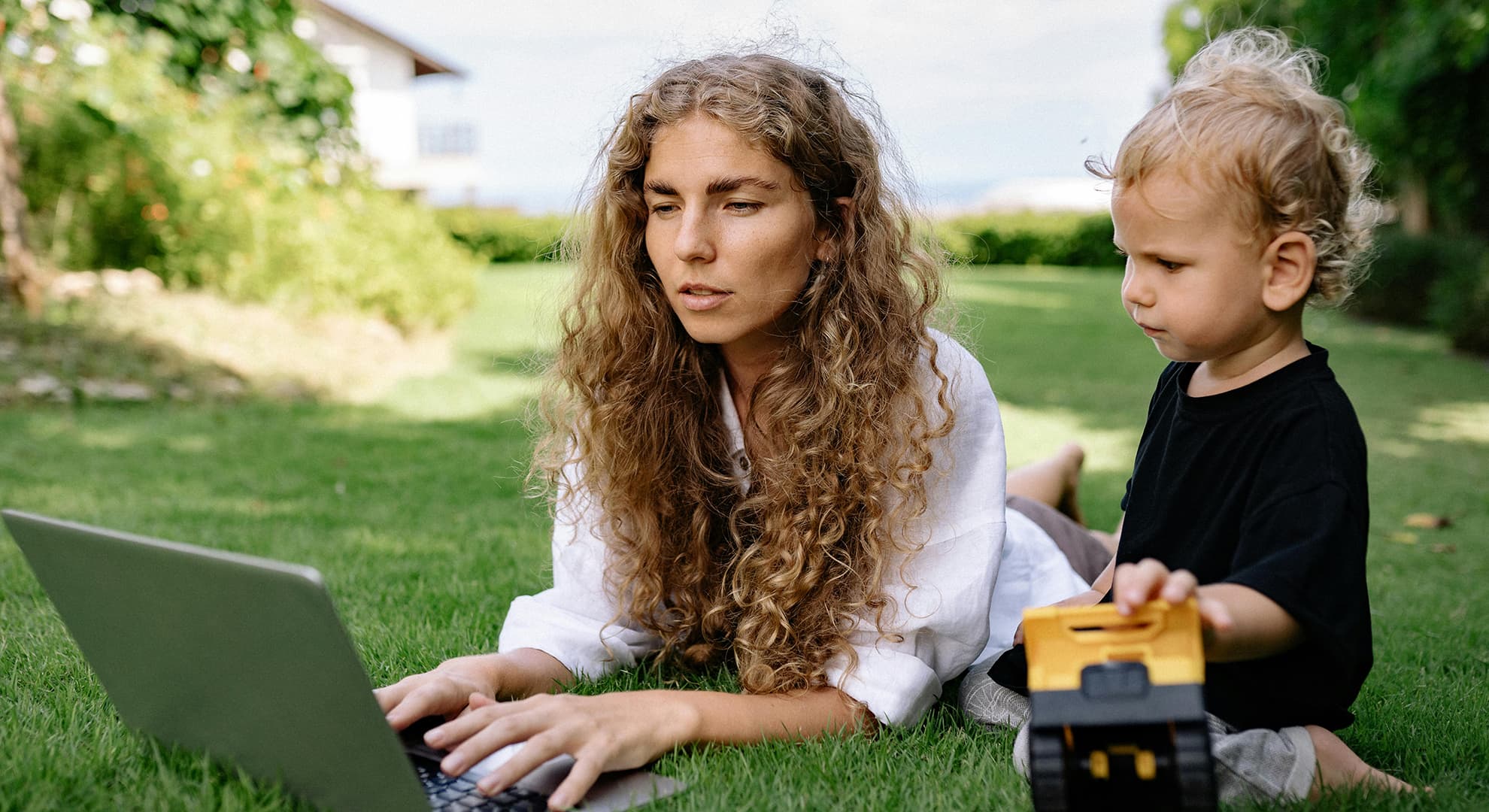 Woman lying on grass with computer and toddler.