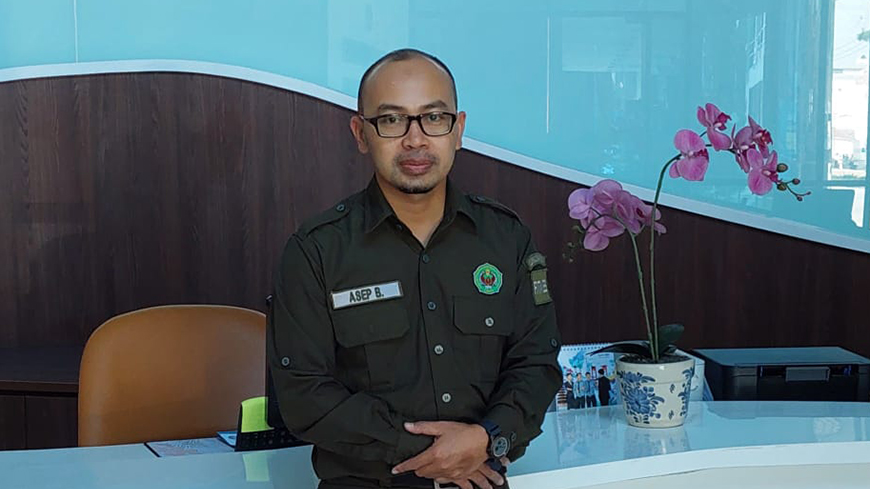 Asep Badruiamaludin stands in front the a reception desk in uniform.