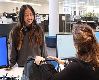 A student returns a laptop to a smiling staff member at Joondalup Campus Library's enquiry desk.